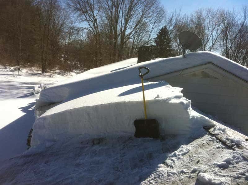 Shovel in front of a wall of at least4 feet of snow on a roof.