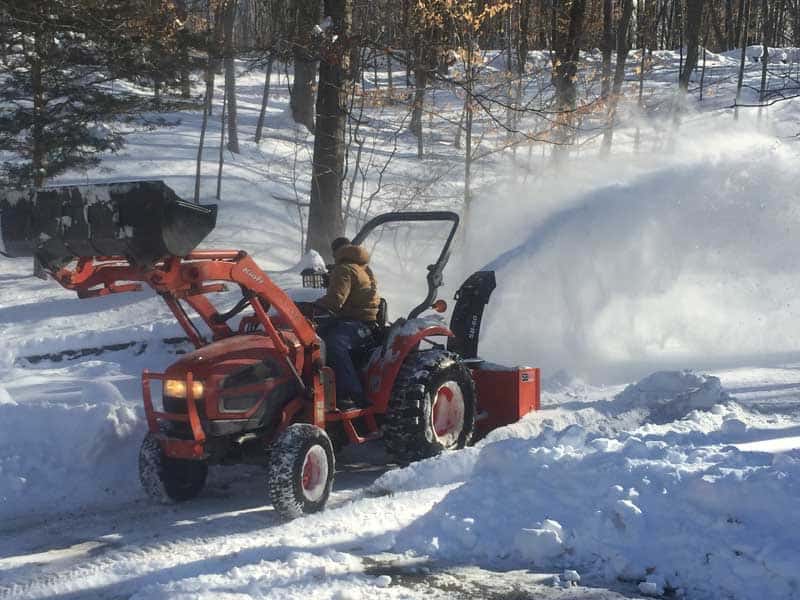 Large snow plow blowing snow off of a driveway.