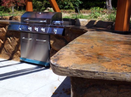 Outdoor kitchen with grill and natural brown stone countertop.
